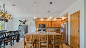 A kitchen with wooden cabinets, a central island, and a dining area with chairs.