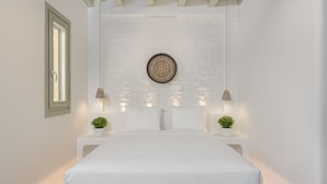 A bedroom with a large bed, two bedside tables with lamps, a decorative wall hanging, and a window with blinds. - Villa TROPICAL OASIS, Kalafatis, Mykonos. (Mykonos)