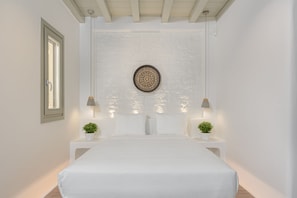 A bedroom with a large bed, two bedside tables with lamps, a decorative wall hanging, and a window with blinds.