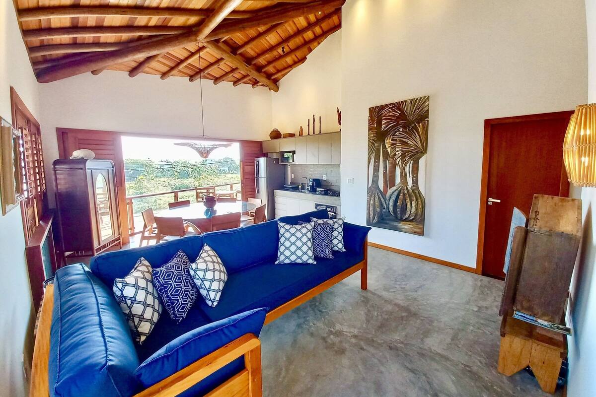 Una sala de estar con un sofá azul, techo de madera y vistas al exterior.
