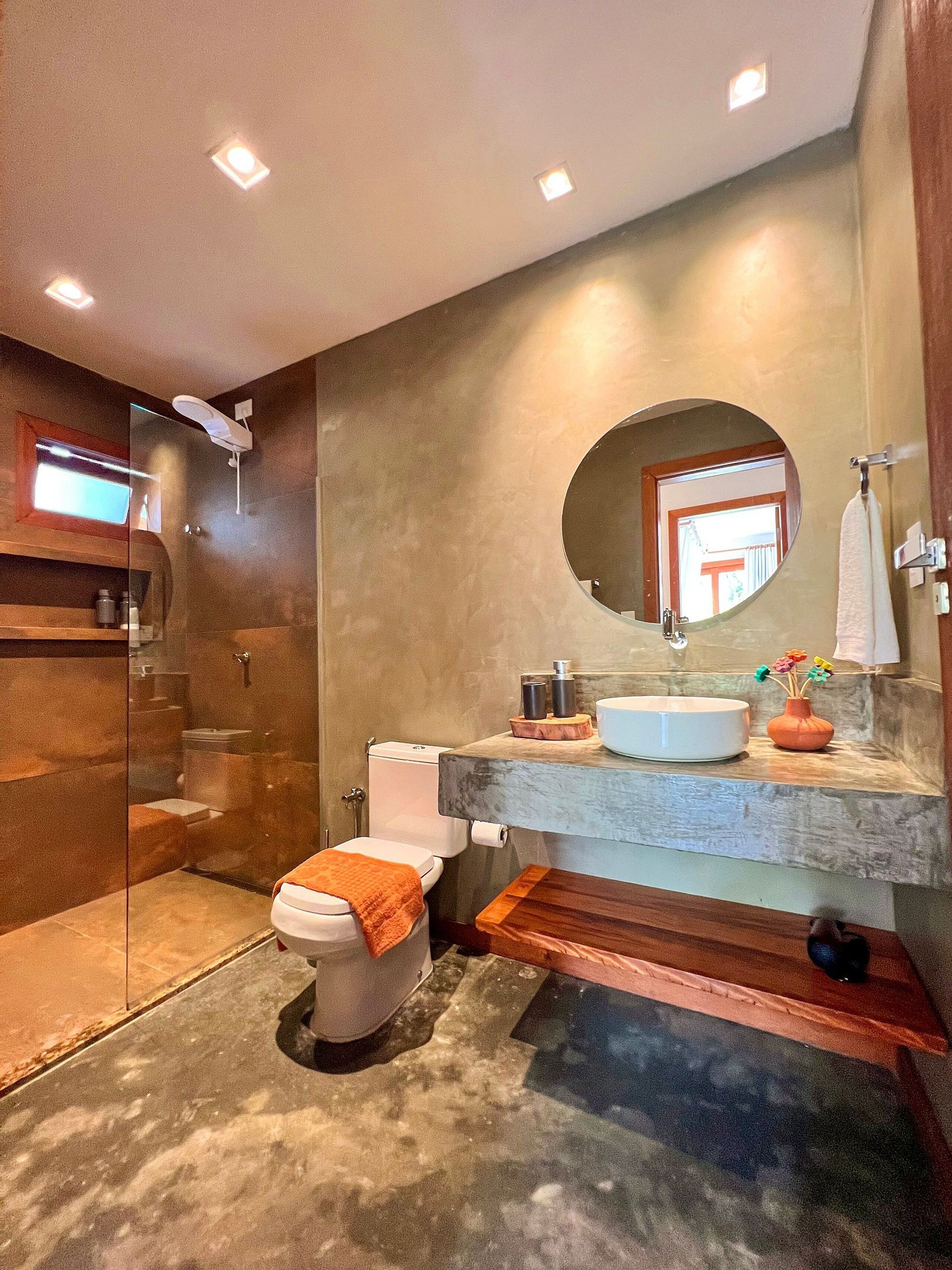 A modern bathroom with a glass-enclosed shower, a white toilet, a sink with a marble countertop, and a round mirror.