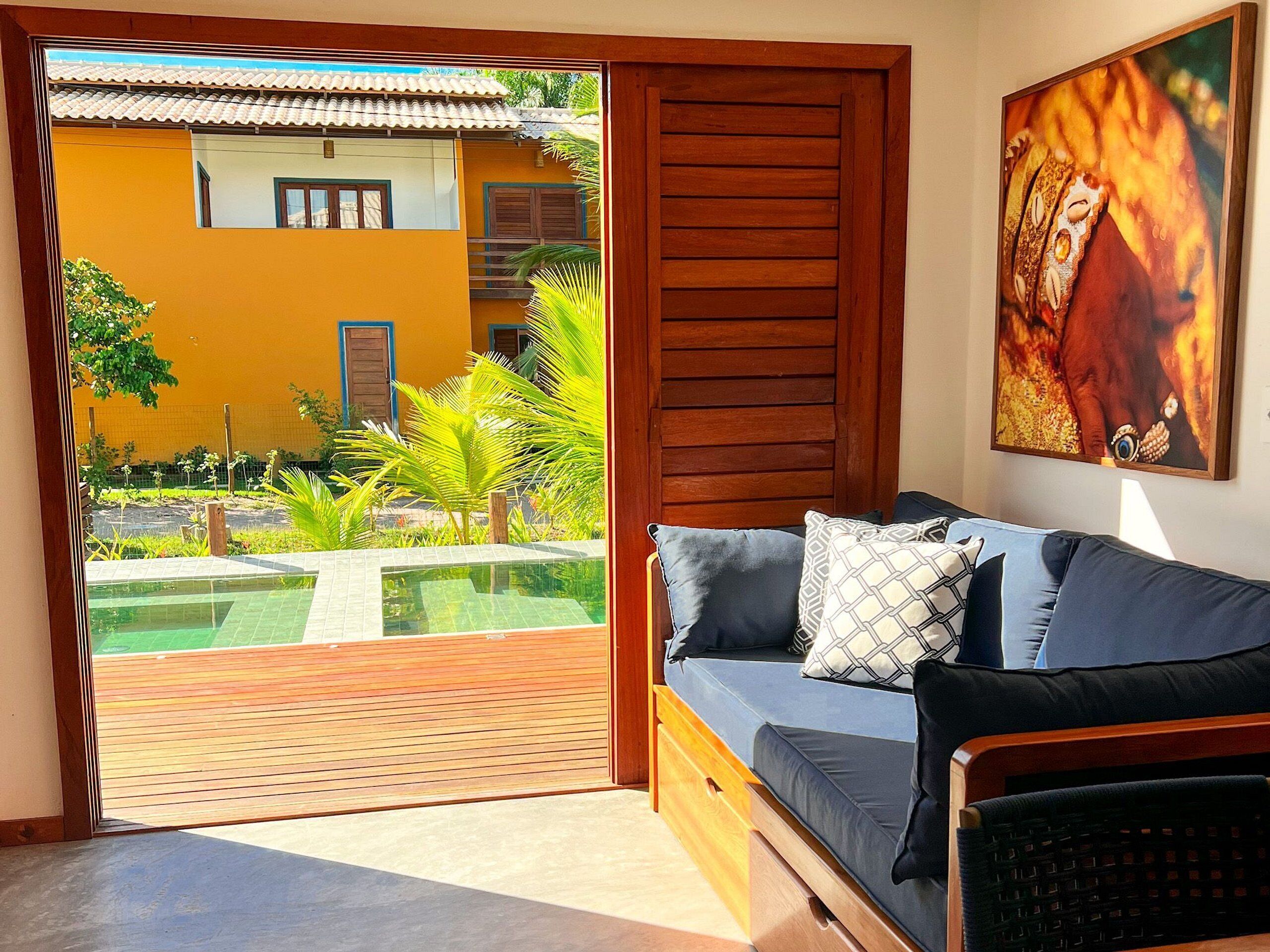 Una habitación con puerta de madera que da a un balcón con piscina, un sofá con cojines y un cuadro en la pared.