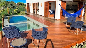 Un área junto a la piscina con terraza de madera, sillones de descanso y una hamaca.