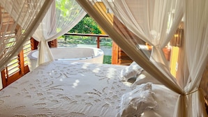 Un dormitorio con una cama grande, una bañera y un balcón con vistas a la vegetación.