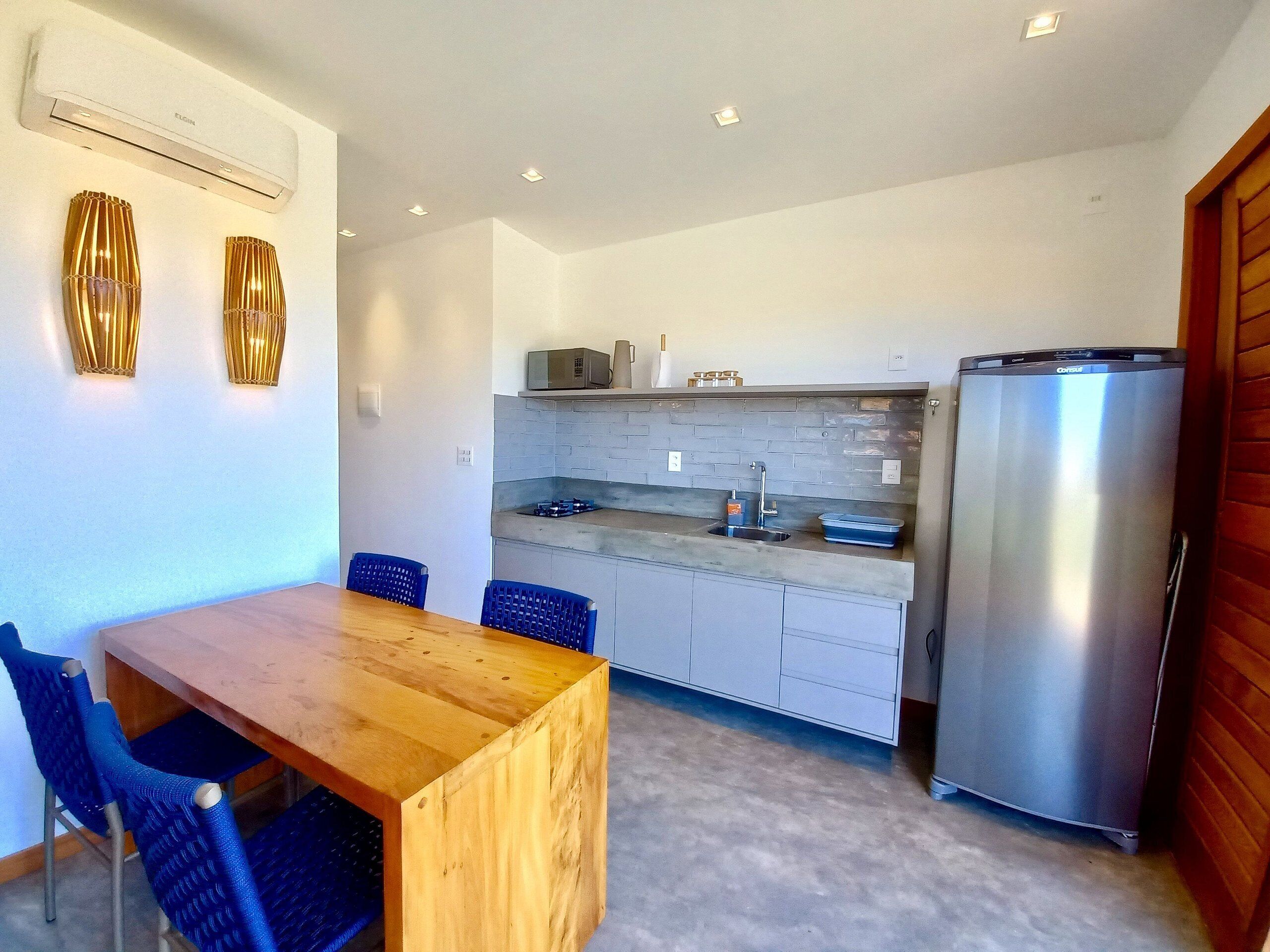A modern kitchen with a wooden dining table, blue chairs, a stainless steel refrigerator, and a microwave.
