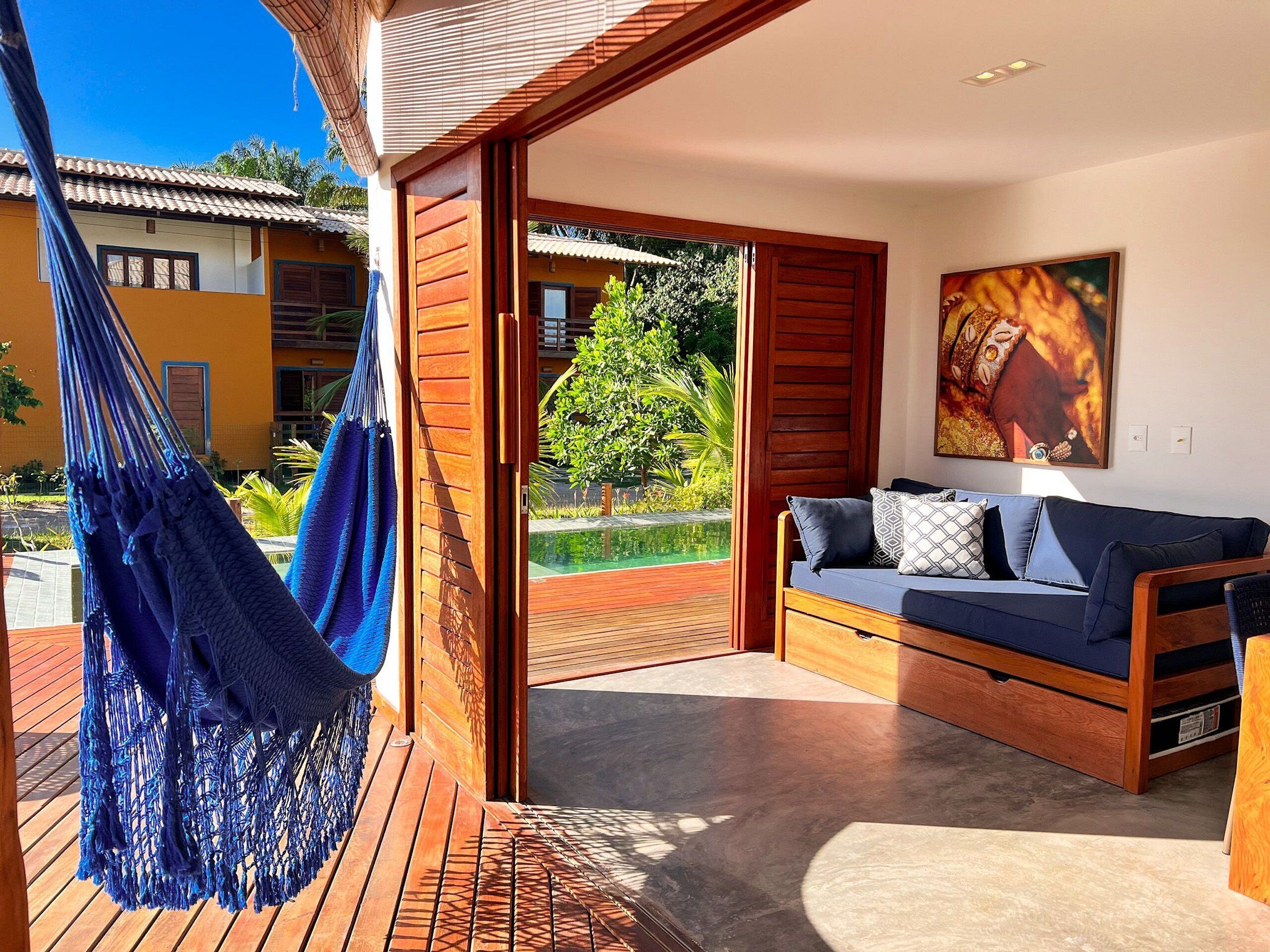 Une pièce moderne avec un plancher en bois, un canapé bleu agrémenté de coussins, un hamac et une grande fenêtre donnant sur un jardin.