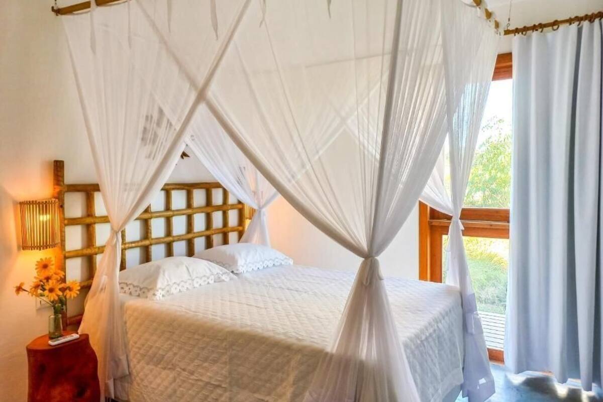 Un dormitorio con cama a dosel, una mesita de noche con lámpara y vistas al exterior.