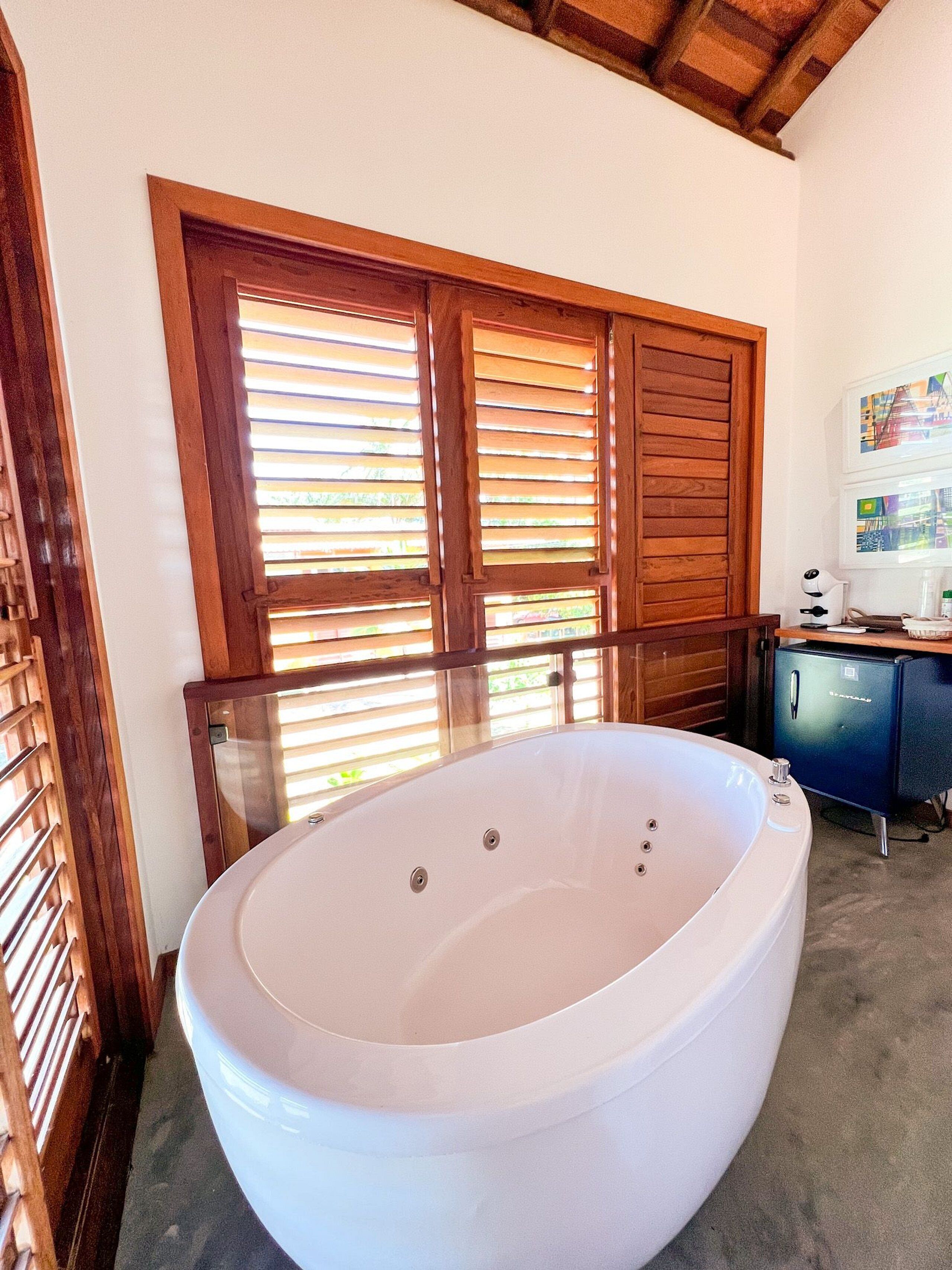 A bathroom with a large freestanding bathtub, wooden shutters, and a small desk with a lamp.