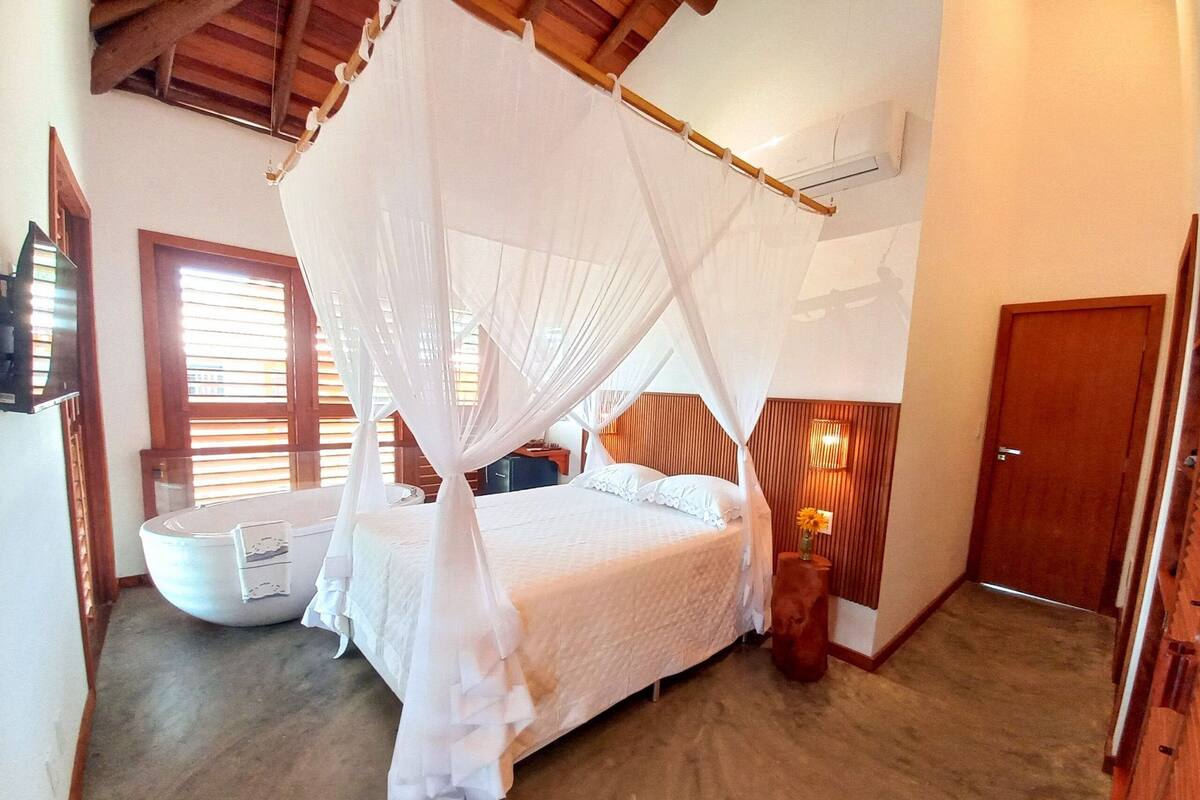 Un dormitorio con cama con dosel, una mesita de noche con un florero y un cabecero de madera.