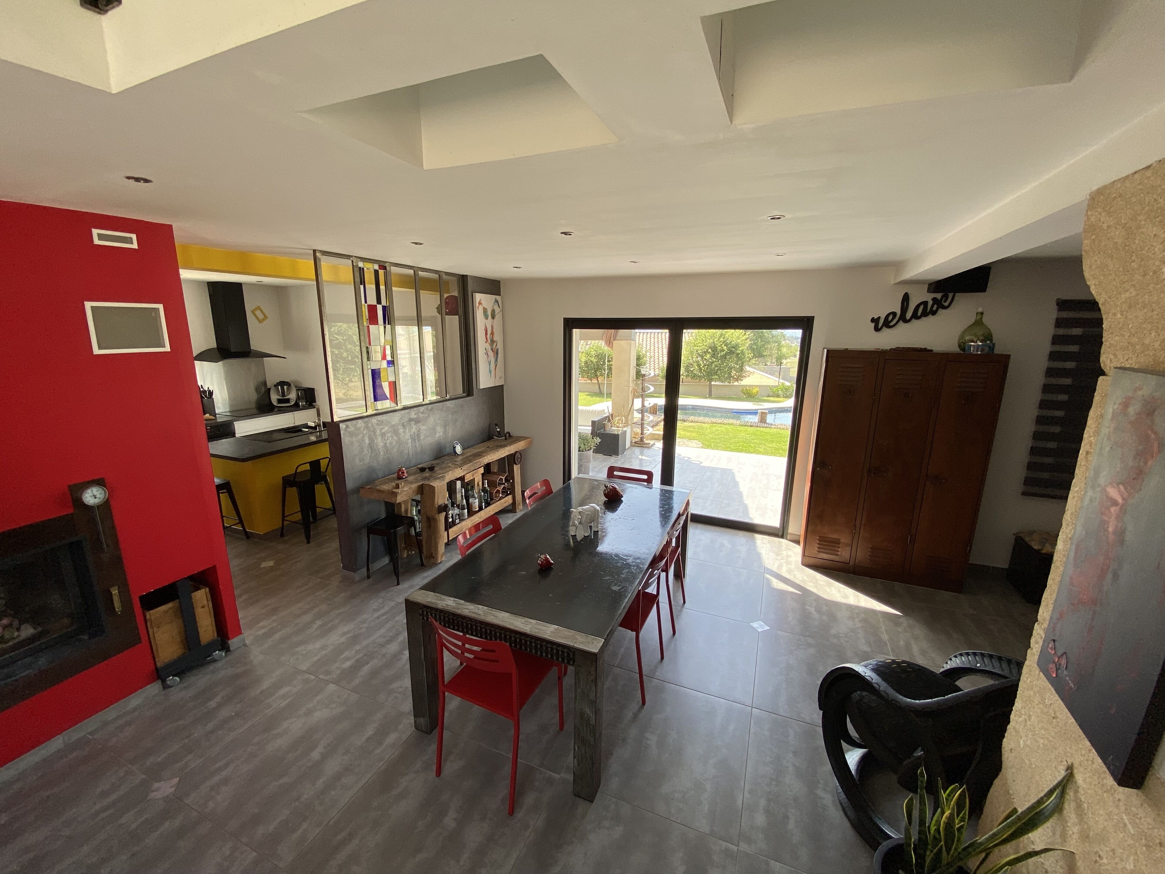 Une cuisine moderne avec un coin repas, un mur rouge et une vue sur l’extérieur.