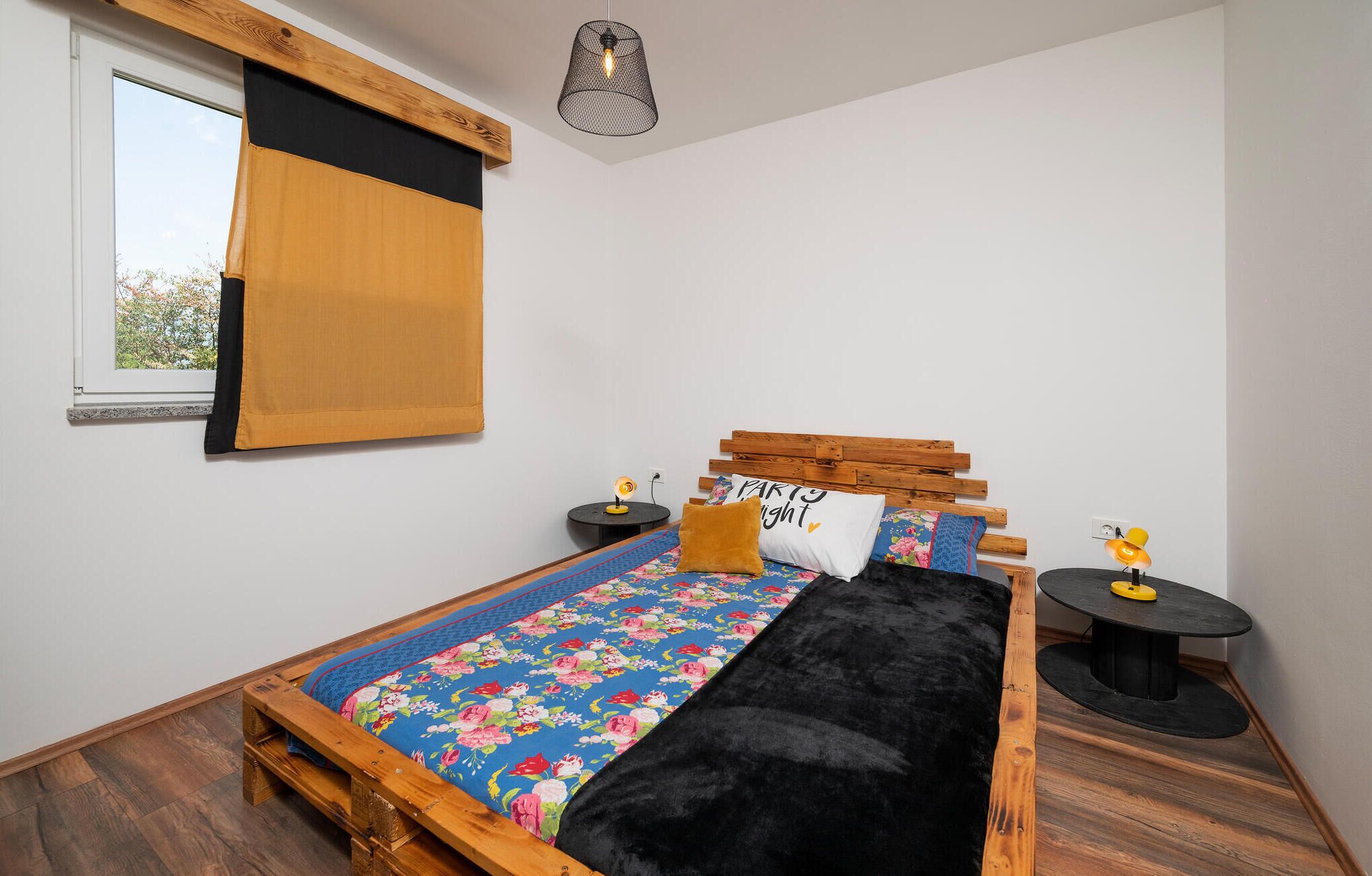 Une chambre à coucher avec un lit en bois, une fenêtre avec un store, un luminaire suspendu et deux tables de chevet avec des lampes.