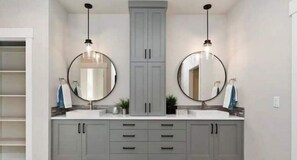 A bathroom with two sinks, grey cabinets, and round mirrors.