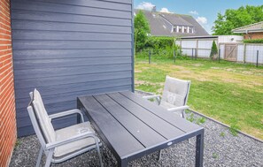 Relax on the patio with a dark table and two comfortable chairs, surrounded by a grassy lawn and a charming wooden fence.