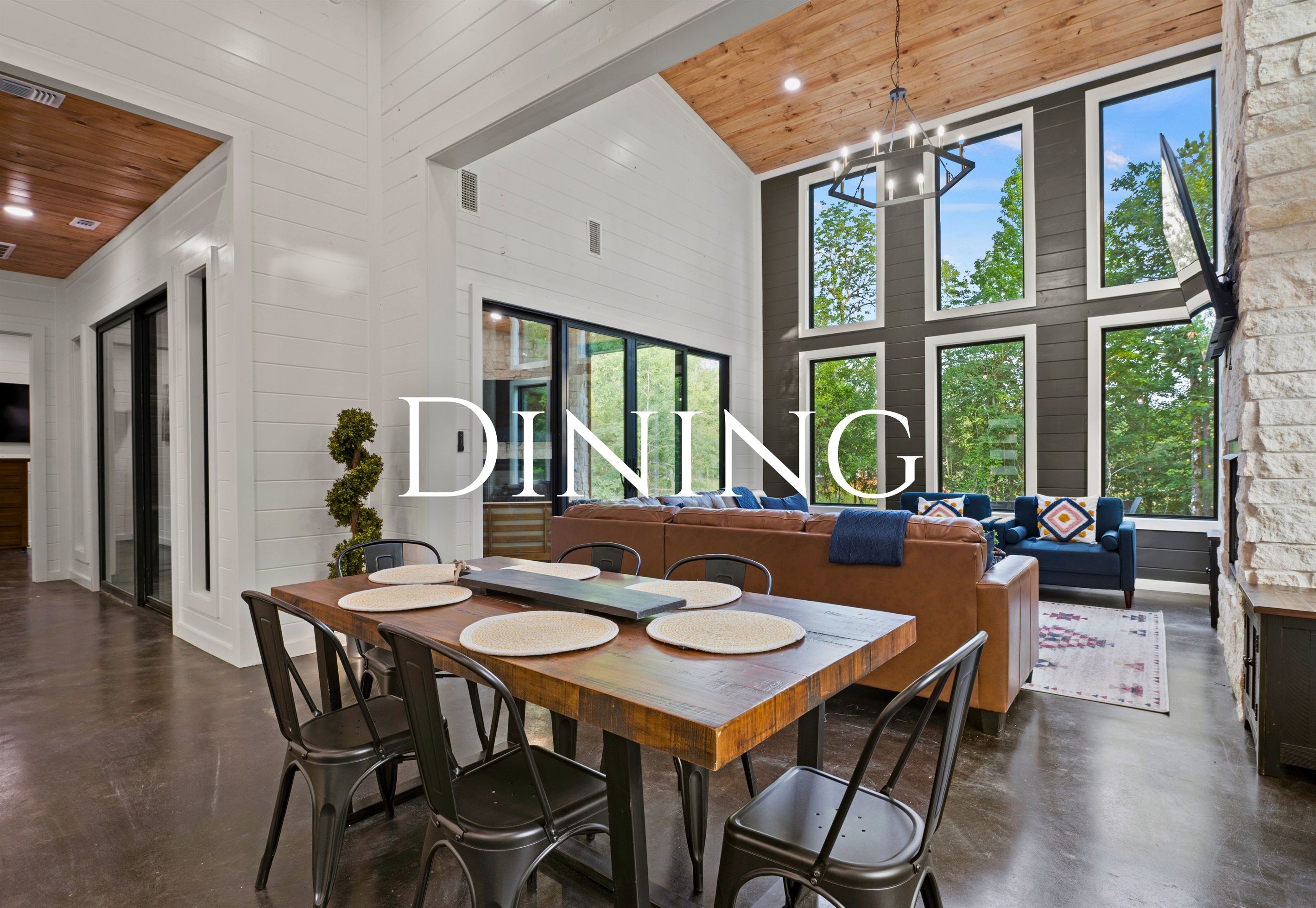A dining area with a wooden table and chairs, a sofa, and a stone wall with windows.