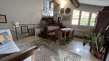 Een ruime woonkamer met een trap, een eettafel met stoelen, een kamerbreed tapijt met dessin en een potplant.