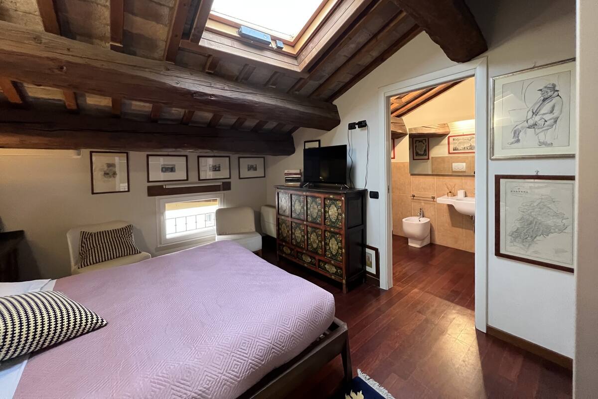 A bedroom with a bed, a television, a wooden cabinet, and a skylight.