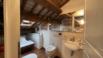 A compact bathroom with a bidet, toilet, and sink. It features wooden beams on the ceiling and a small window.