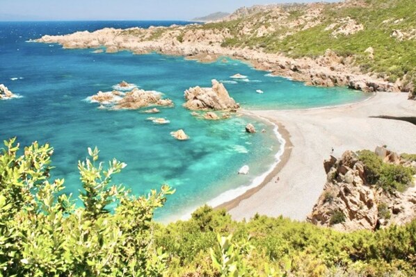 A coastal landscape with clear turquoise waters, rocky formations, and a sandy beach.