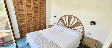 A bedroom with a large bed, a wooden wardrobe, a small bedside table, and a wall-mounted light.