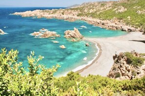 Un paysage côtier caractérisé par une eau turquoise cristalline, des formations rocheuses et une plage de sable.