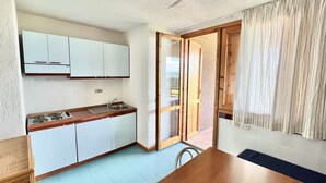 Una cucina compatta con mobili bianchi, un piano di lavoro in legno e una porta a vetri scorrevoli che dà su uno spazio esterno.