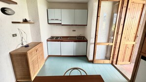 Una cucina compatta con mobili bianchi, un tavolo da pranzo in legno e una porta scorrevole in vetro che dà su uno spazio all'aperto.