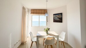 Un comedor con una mesa, sillas, una lámpara colgante, un ventanal con vista al mar y un cuadro en la pared.