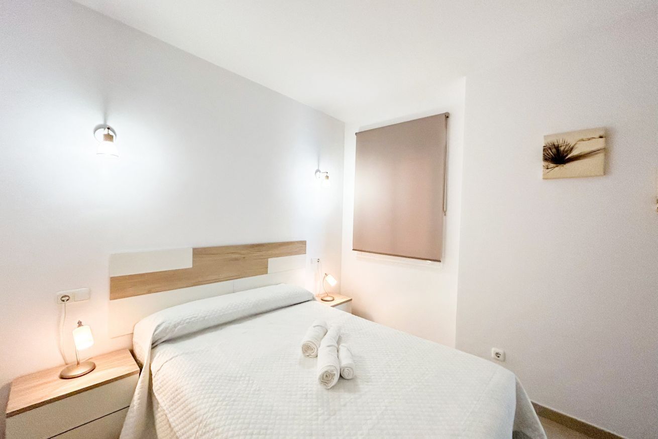 Une chambre d’hôtel bien aménagée, avec un lit, deux tables de chevet dotées de lampes, une œuvre d’art accrochée au mur et une fenêtre avec un store.