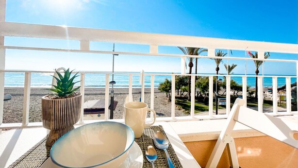 Un balcón con vistas despejadas a la playa, una mesa con un bol, una taza y una planta.