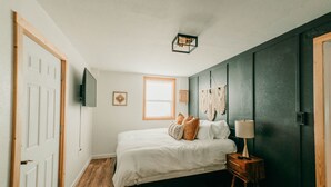 A bedroom with a bed, a nightstand, a lamp, a TV, and a window. - Modern cottage centrally located with private access to the Rogue River! (Grants Pass)