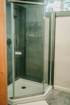 Une cabine de douche fermée par des parois en verre, avec un receveur blanc et un mur recouvert de carreaux.