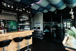 Una zona de bar con taburetes, estantes llenos de botellas y un cartel que dice 'The bar's 24 hour'.