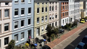 Une rangée de maisons de ville aux couleurs vives, une rue pavée, une voiture jaune garée sur le bord et un ciel bleu azur.