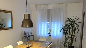 Un coin repas avec une table en bois, des chaises blanches, une suspension et une plante en pot.
