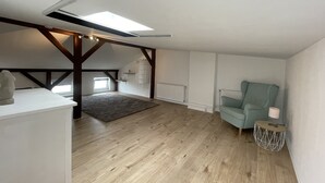 Une chambre mansardée avec un puits de lumière, des poutres en bois, un fauteuil vert, une petite table ronde et un radiateur.