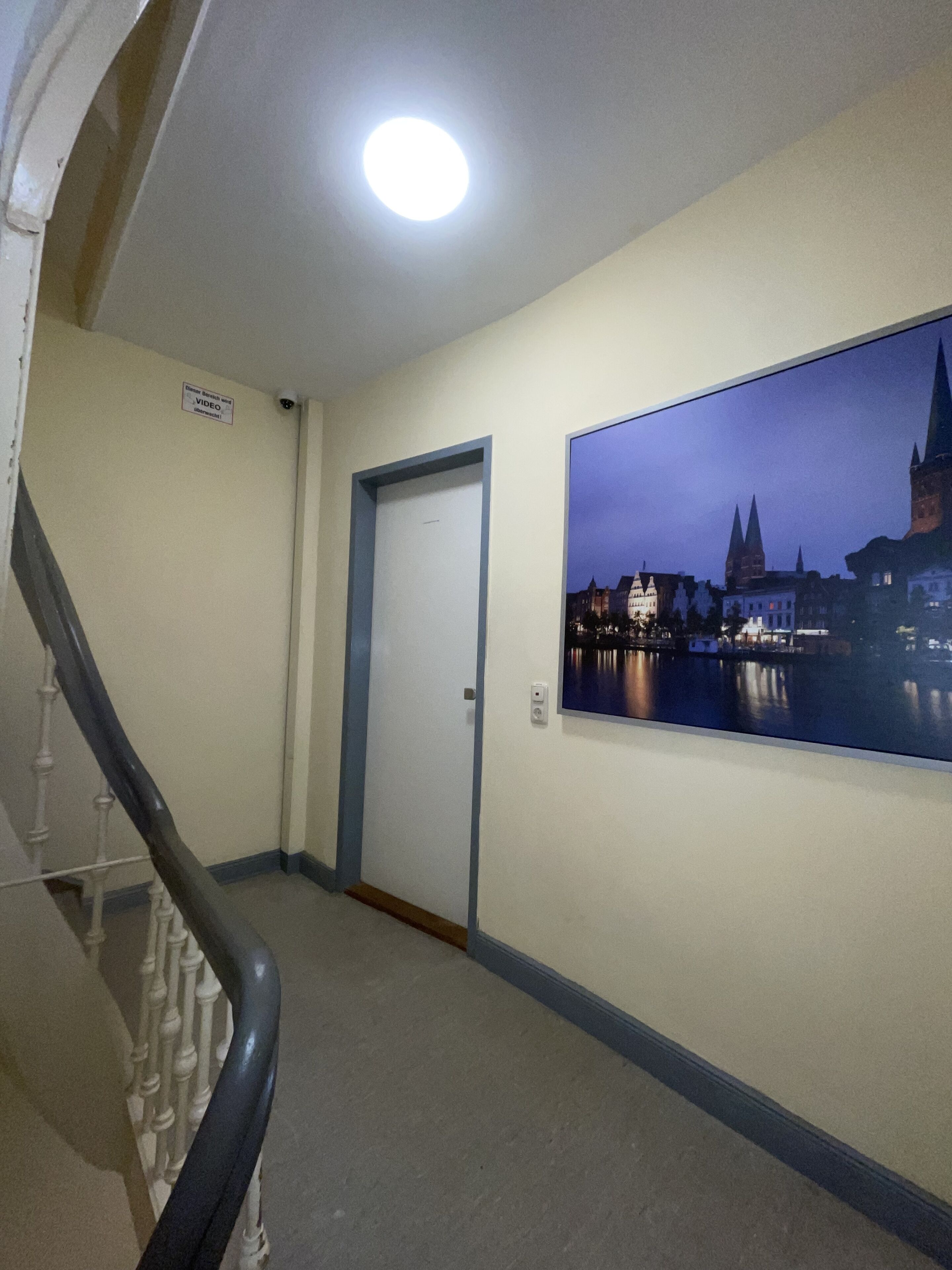 Ein Flur mit Treppe, einer Tür und einem Stadtbild an der Wand.