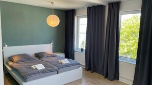 Une chambre à coucher moderne, avec un lit, des tables de chevet, un luminaire suspendu et une fenêtre avec des rideaux.