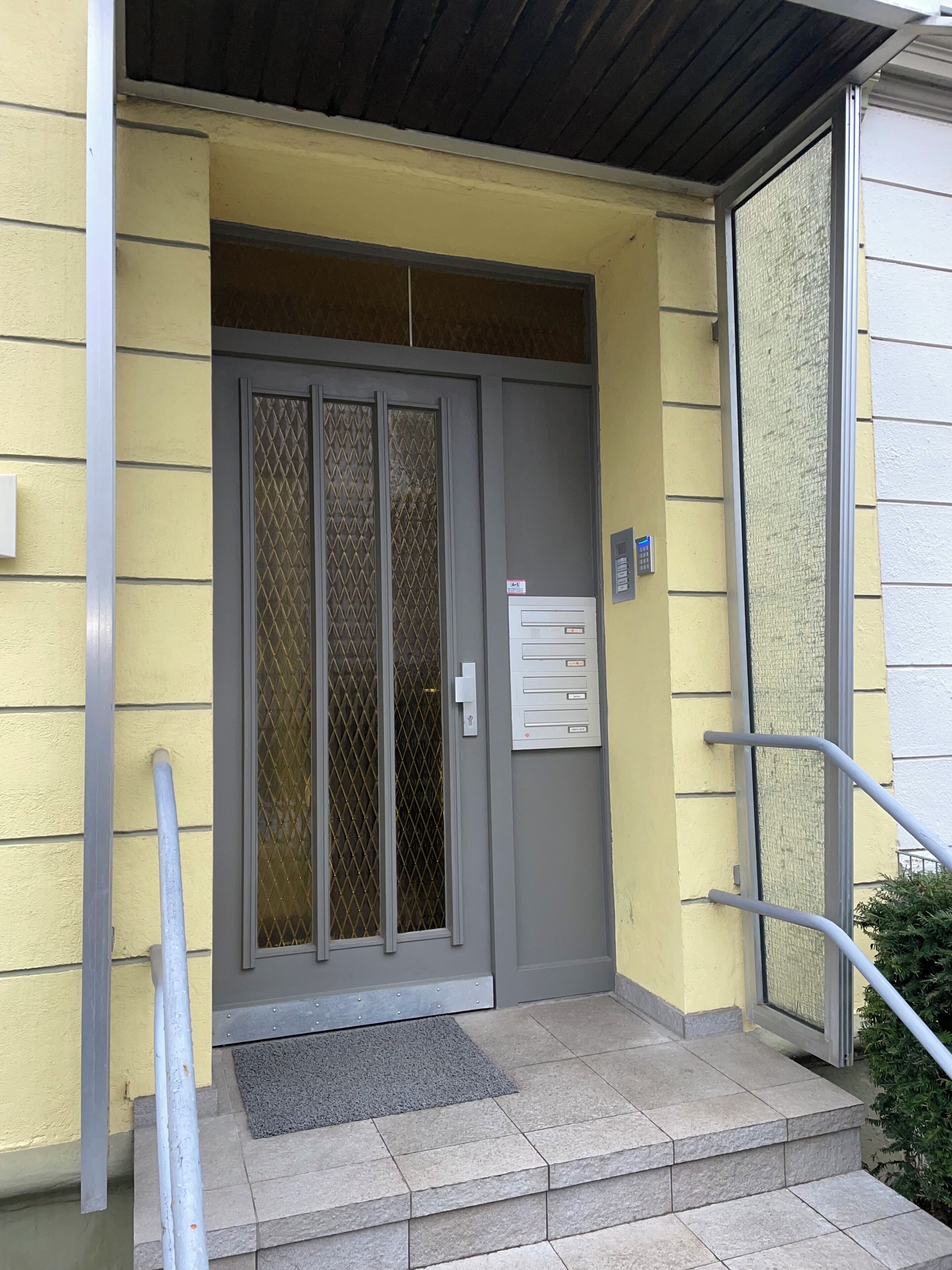 A building entrance with a grey door, a metal mail slot, and a grey mat.