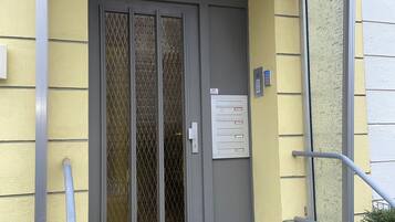 A building entrance with a grey door, a metal mail slot, and a grey mat.