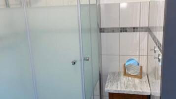 A bathroom with a glass shower enclosure, a wooden vanity with a mirror, and tiled walls.