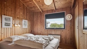 Un dormitorio con paneles de madera, una cama, un ventanal y luces fijadas a la pared.