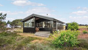 Una cabaña moderna con amplio ventanal, terraza de madera y chimenea.