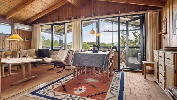 Interior acogedor de una cabaña con comedor, pisos de madera y ventanas amplias que ofrecen vistas al exterior.