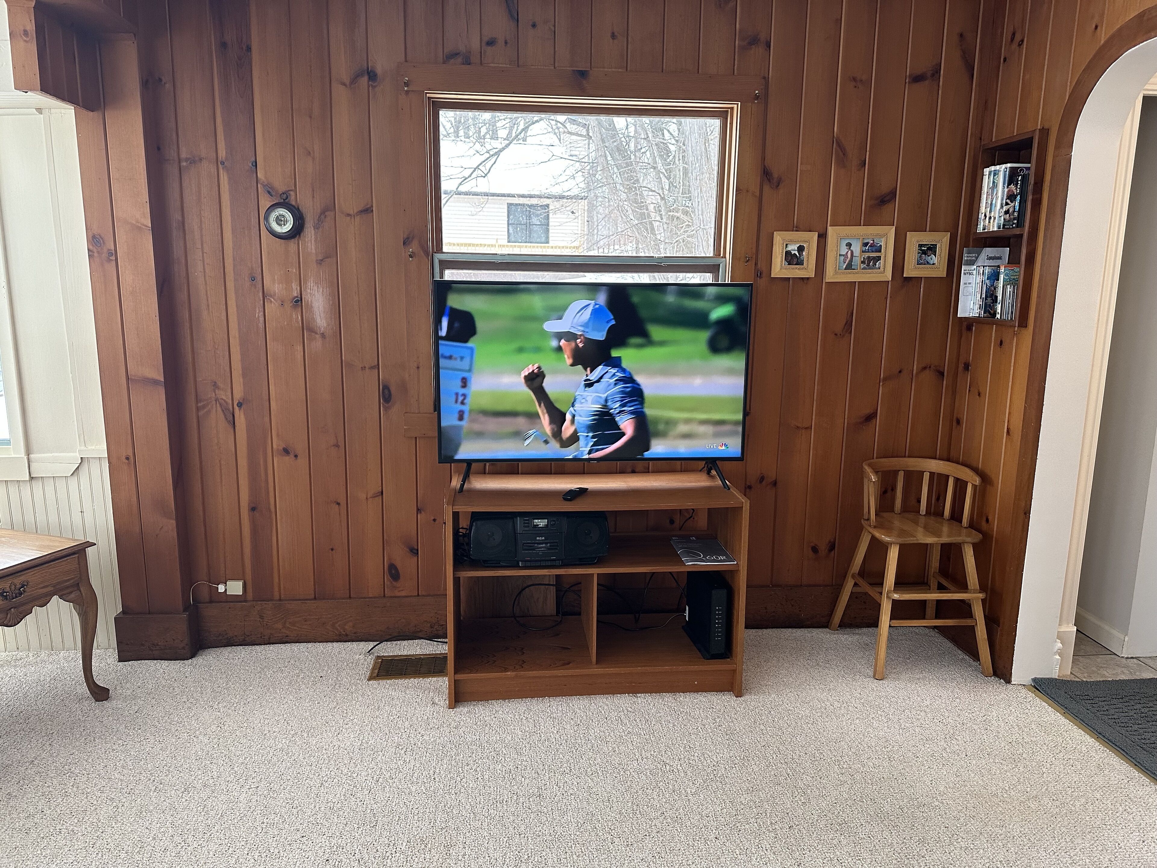 Quarto com painéis de madeira, uma televisão sobre suporte de madeira, uma mesa pequena e uma cadeira.