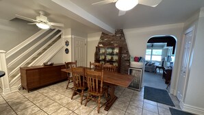 Un comedor con una mesa y sillas de madera, una cocina con pared de ladrillo y una escalera que sube a otro nivel.