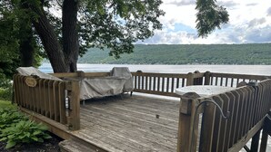 Una terraza de madera con un banco, con vistas a un lago y una ladera boscosa al fondo.