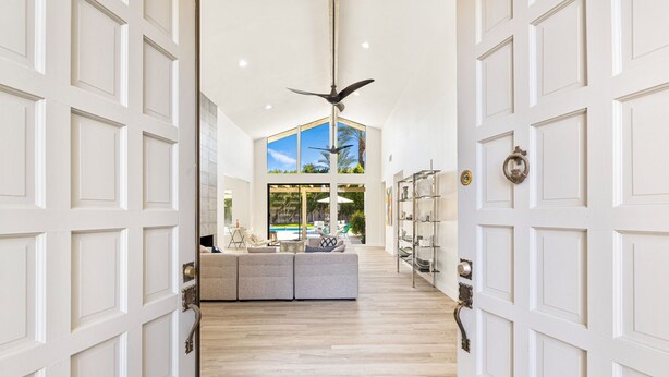A spacious hallway with a high ceiling, a ceiling fan, and a view of a balcony with outdoor furniture. - Presidential Vacation Retreat (Rancho Mirage)