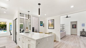 A modern kitchen with a marble island, white cabinetry, and pendant lighting. - Presidential Vacation Retreat (Rancho Mirage)