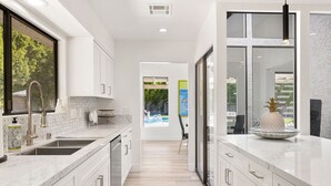 A modern kitchen with white cabinetry, a large island, and a view of the outdoors. - Presidential Vacation Retreat (Rancho Mirage)