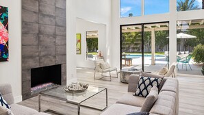 A spacious living room with a fireplace, comfortable seating, and large windows offering a view of the outdoors. - Presidential Vacation Retreat (Rancho Mirage)